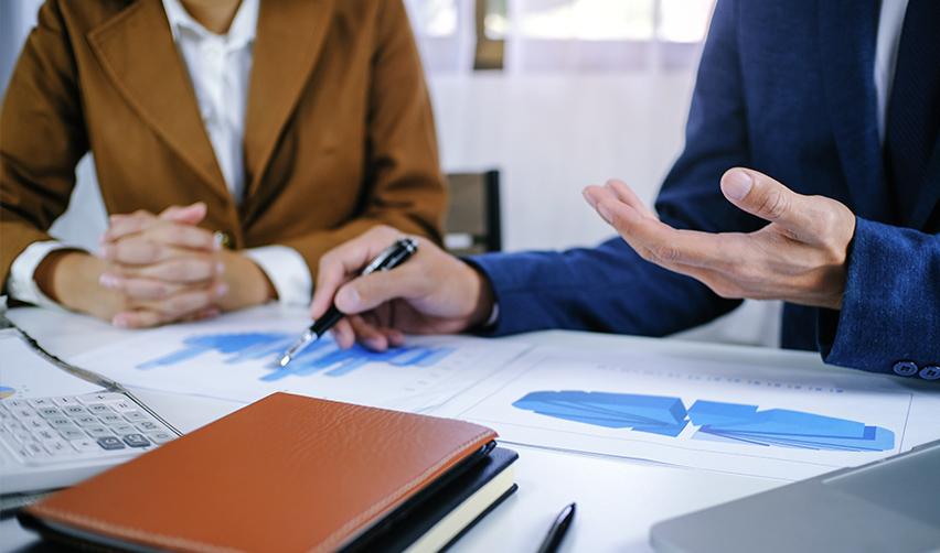 An EB5 financial advisor explaining the details of the business venture to an alien investor, with business graphs and documents on the desk.