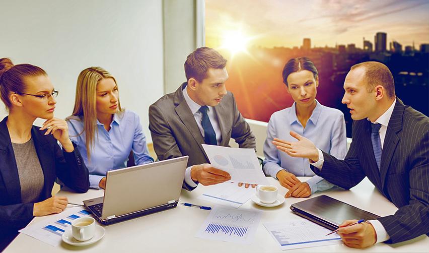 A group of Eb5 experts sitting around an office desk with laptops and business documents, discussing the capital investment of foreign nationals under the regional center program.