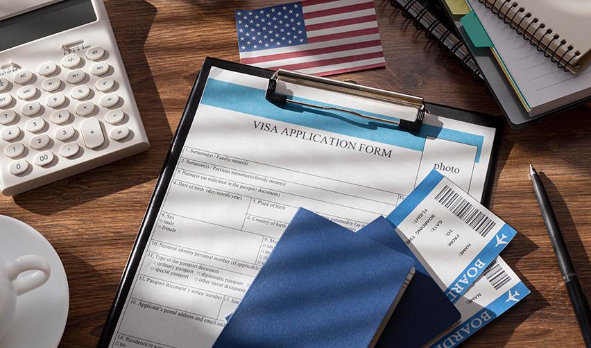 An immigrant visa application form on a desk with passports, a calculator and plane tickets.