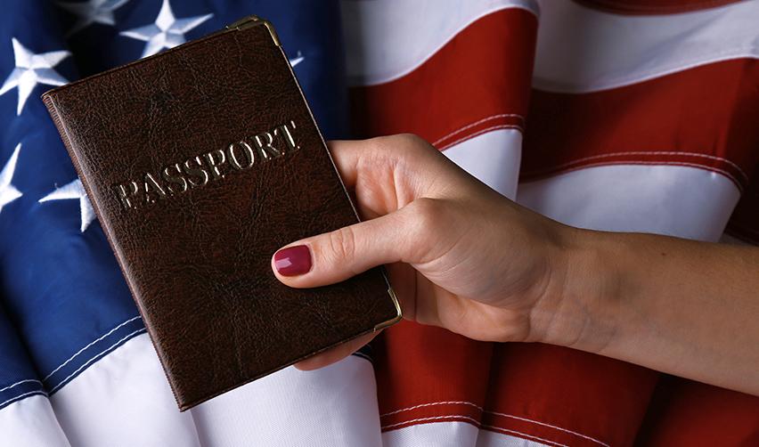 An alien entrepreneur holding a passport up in front of the American flag.