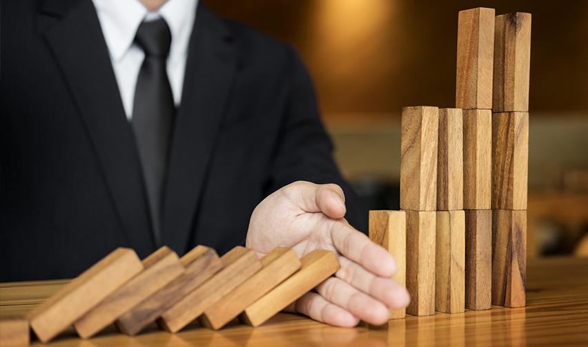 A hand stopping a domino effect, symbolizing risk mitigation in regional center investments.