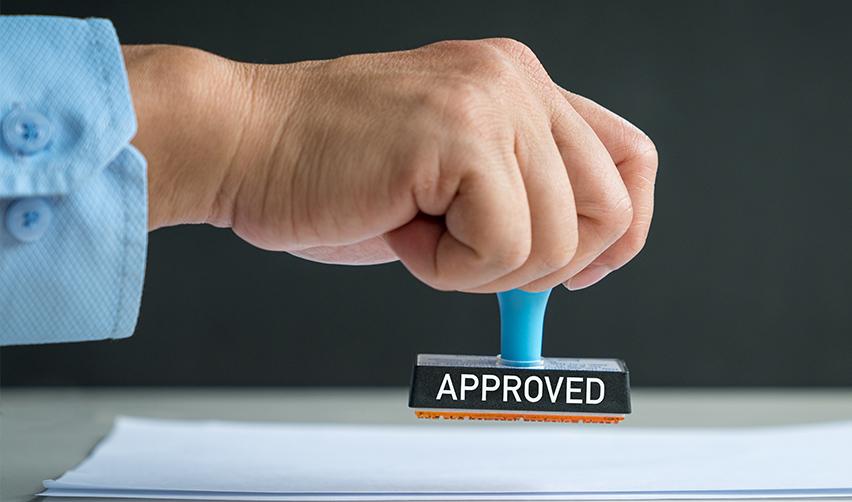 A hand stamping a regional center investment document with a stamp that reads approved on it.