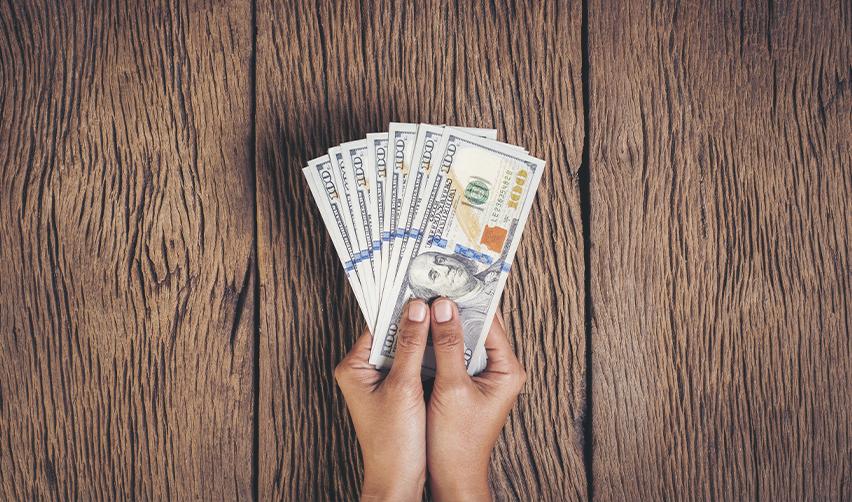 Two hands holding a stack of dollars.