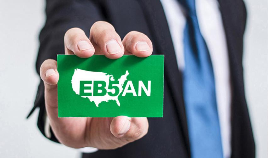 Close-up of a hand holding a green card with the EB5AN logo on it.