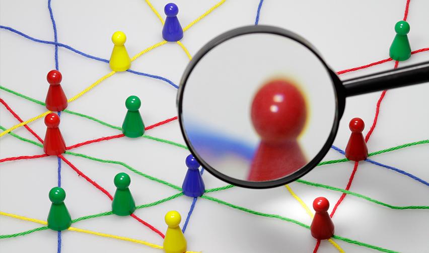 A magnifying glass over figurine pins connected to each other by colorful threads.