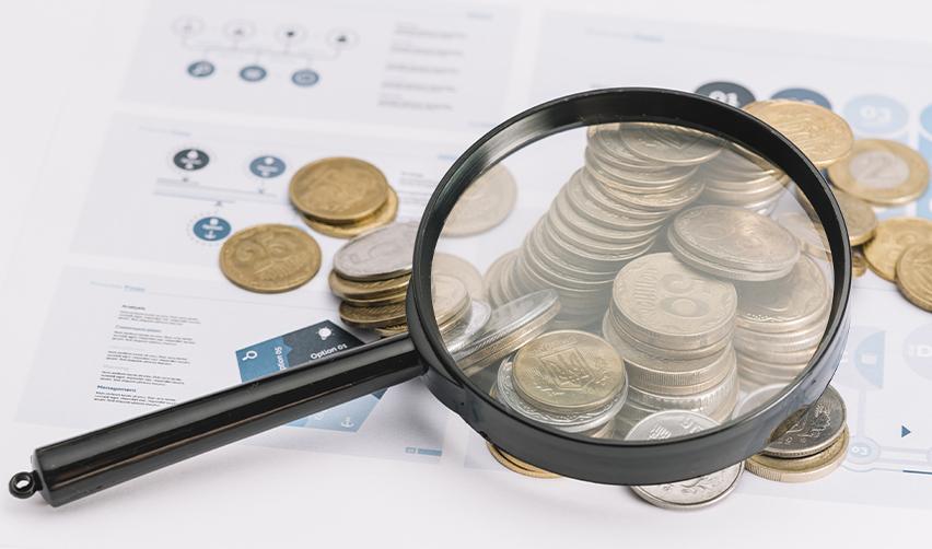 A magnifying glass on a stack of coins.