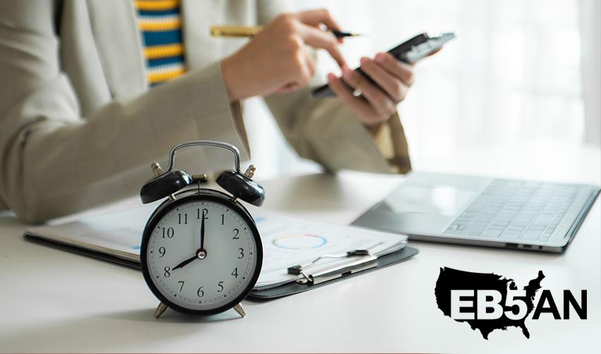 An EB5 investor working on some visa application documents behind an alarm clock, next to the EB5AN logo.