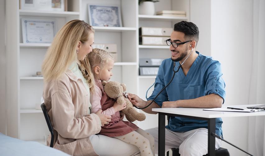A doctor examining a child on her mother's lap, symbolizing U.S. healthcare access for immigrant families.