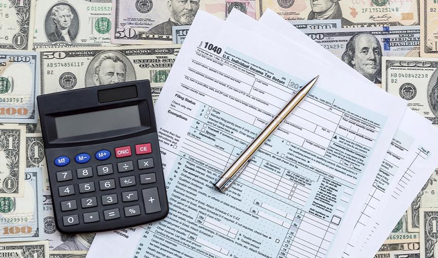 A calculator and Form 1040 documents on top of U.S. dollars.