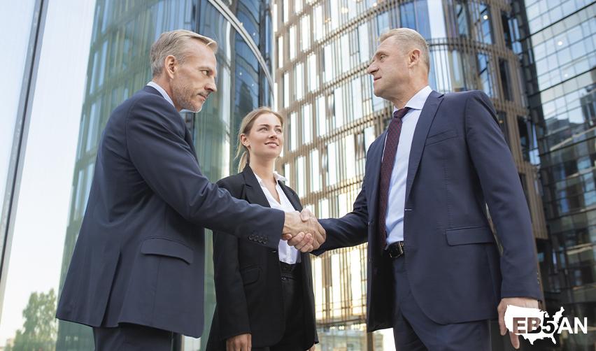 A group of EB5 industry professionals shaking hands with an alien entrepreneur, with the EB5AN logo on the corner.