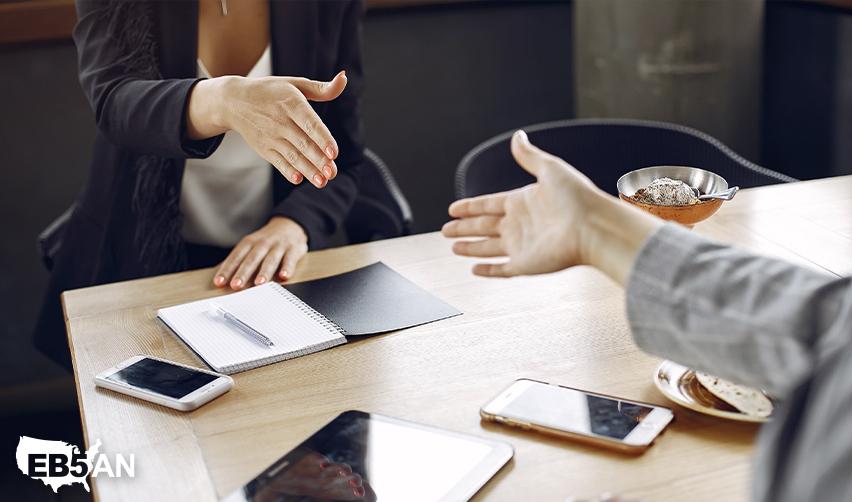 An EB5 investor shaking hands with a regional center managing partner at an office, with the EB5AN logo on the corner.