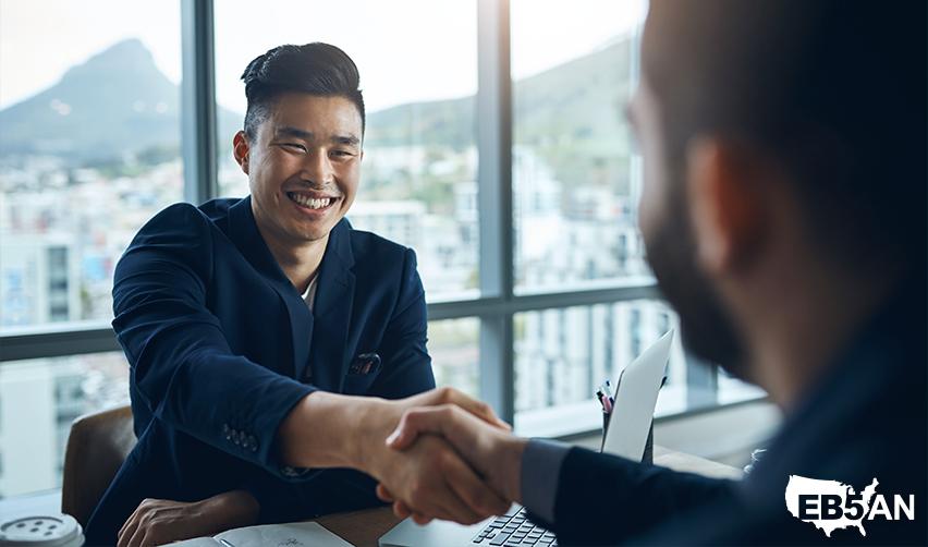 A Singaporean investor completing his US visa applications, shaking hands with an EB5 regional center professional with the EB5AN logo on the corner.