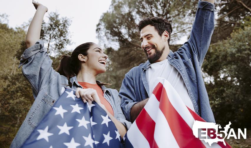 A couple of EB5 green card holders celebrating outdoors with U.S. flags, with the EB5AN logo on the corner.