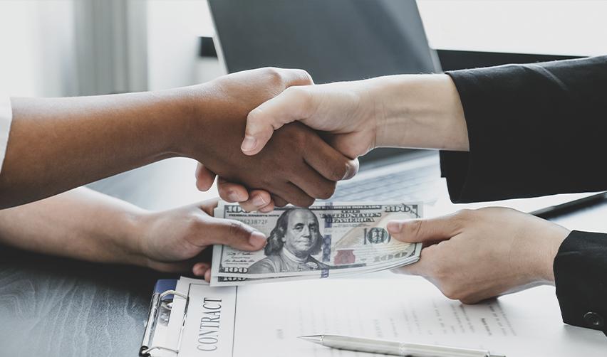 Two people shaking hands while handing each other U.S. dollars, symbolizing the loan terms for a real estate project.