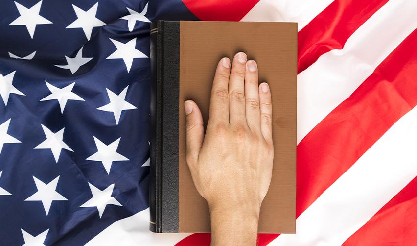 An EB5 green card holder's hand on a book on top of the U.S. flag, symbolizing citizenship by investment in the U.S.