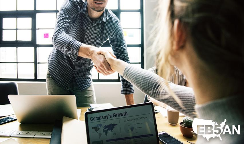 An EB5 targeted employment area investor shaking hands with a regional center principal, with the EB5AN logo on the corner.