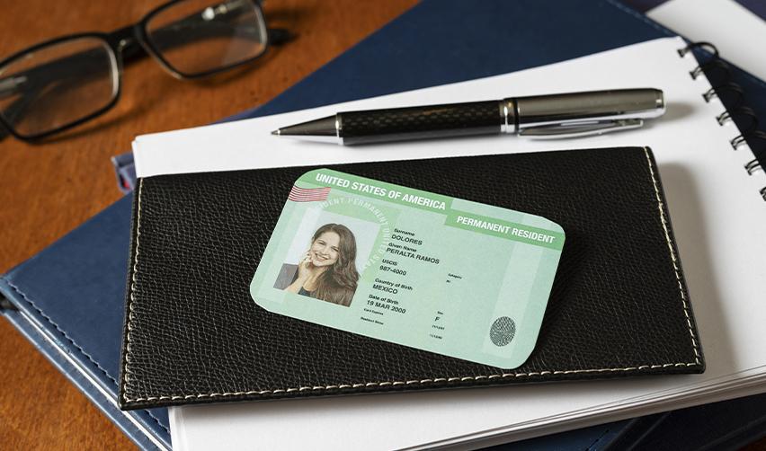 A United States Permanent Resident Card (Green Card) placed on a black leather notebook with a pen and reading glasses, illustrating the benefits of EB5 immigration and permanent residency in the U.S.