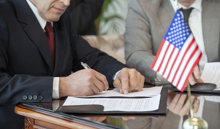 Close-up of a businessperson or immigration attorney signing documents with an American flag on the table, representing legal procedures for obtaining a U.S. Green Card through the EB5 program.