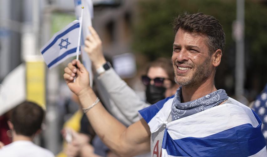 Israeli EB5 investor smiling and waving a national flag at a public event.