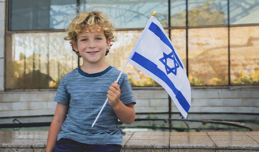 A cheerful Israeli child waves an Israeli flag, representing families navigating consular processing for immigration while living outside the United States and exploring options to apply for a Green Card.