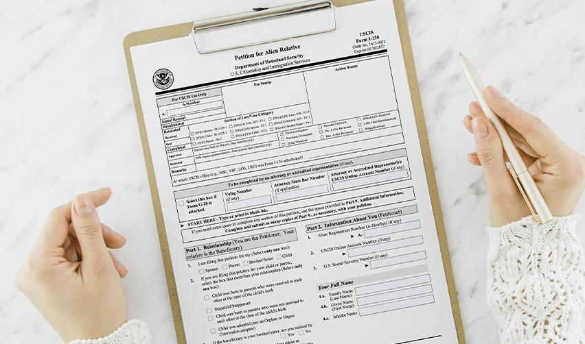 A close-up of hands holding a clipboard with a U.S. Citizenship and Immigration Services (USCIS) petition form for an alien relative, an essential document in the visa application process for those pursuing family-based immigration.