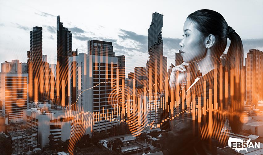 Businesswoman thinking in front of a modern city skyline and the EB5AN logo with financial data overlays, reflecting economic opportunity and the motivation behind EB5 investments for international entrepreneurs.