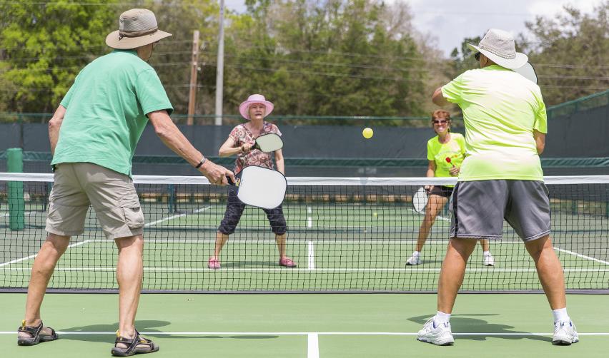 Four older adults playing doubles pickleball on an outdoor court, showcasing the active, social lifestyle available to residents at the Twin Lakes EB5 project sponsored by EB5AN.