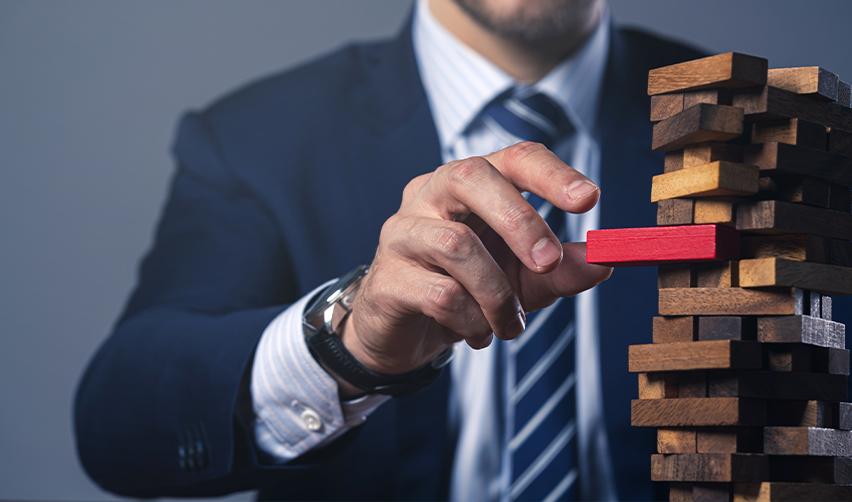A businessperson symbolizing financial risk management in EB5 investments by removing a red block from a Jenga tower.