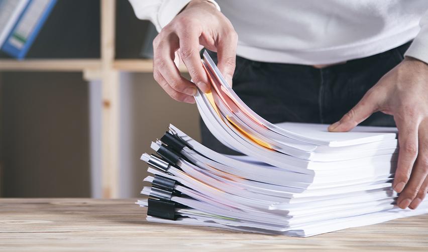 Stack of EB5 source of funds documents being organized by hand, representing detailed USCIS paperwork preparation and financial evidence submission.