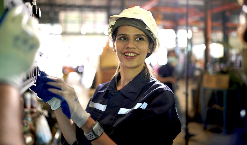 Smiling female worker in protective gear at an industrial site, representing EB5-supported employment opportunities in U.S. manufacturing and skilled labor sectors.