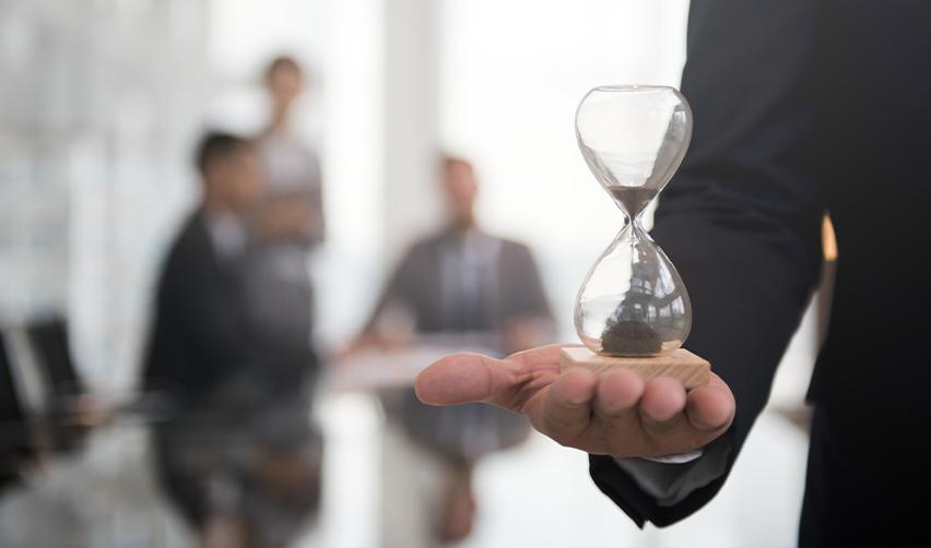 A close-up of a businessman holding an hourglass in a boardroom, symbolizing the urgency of filing EB5 petitions before the fiscal year ends.
