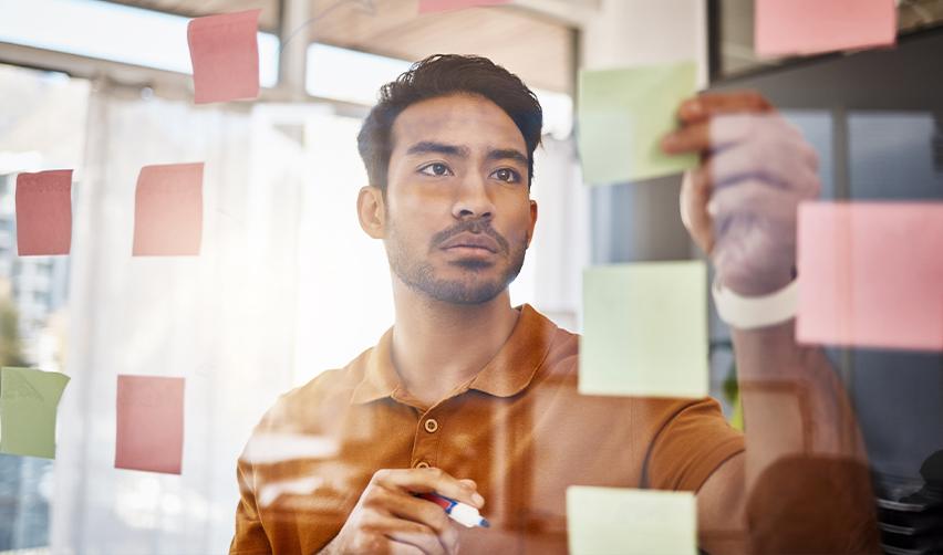 A focused man organizing colorful sticky notes on a glass board, depicting strategic planning for choosing the right EB5 project with the help of EB5AN.