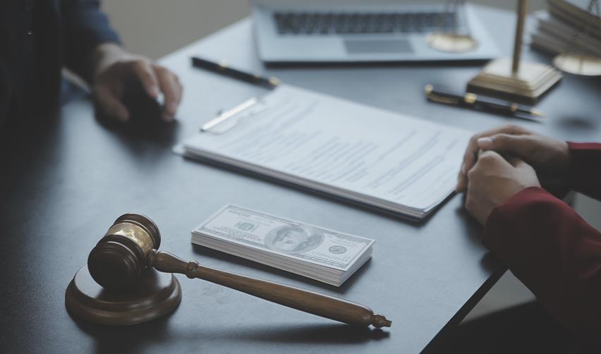 Gavel, cash stack, and legal paperwork on a desk in front of two people, illustrating the importance of EB5 legal guidance, source of funds review, and attorney consultations.