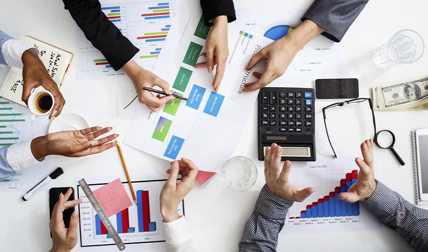Business team collaborating with charts, graphs, and calculators on a desk, representing EB5 investors comparing financial options and structuring their immigration investment strategy.