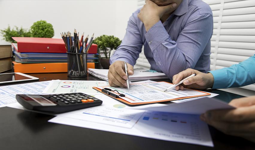 Two professionals reviewing financial documents with a calculator and charts, representing EB5 investors preparing source of funds records for their immigration petition.