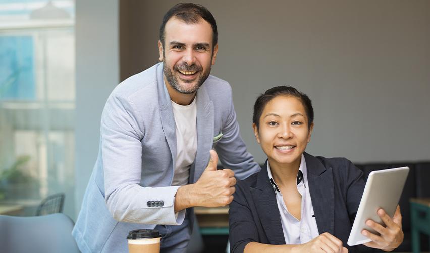 Two professionals smiling and giving a thumbs up while reviewing documents on a tablet, symbolizing EB5 investors gaining confidence with the support of trusted advisors.