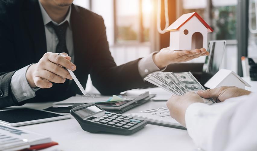 Close-up of two people exchanging cash and documents with a small model house on the table, symbolizing EB5 real estate financing, cash flow, and exit planning.