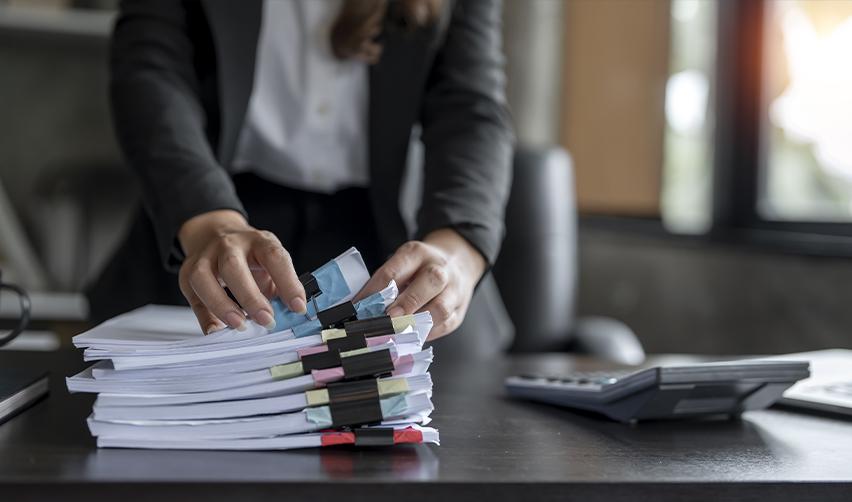 Businesswoman organizing stacks of clipped documents on a desk, illustrating the detailed paperwork required for EB5 source of funds and path of funds documentation.