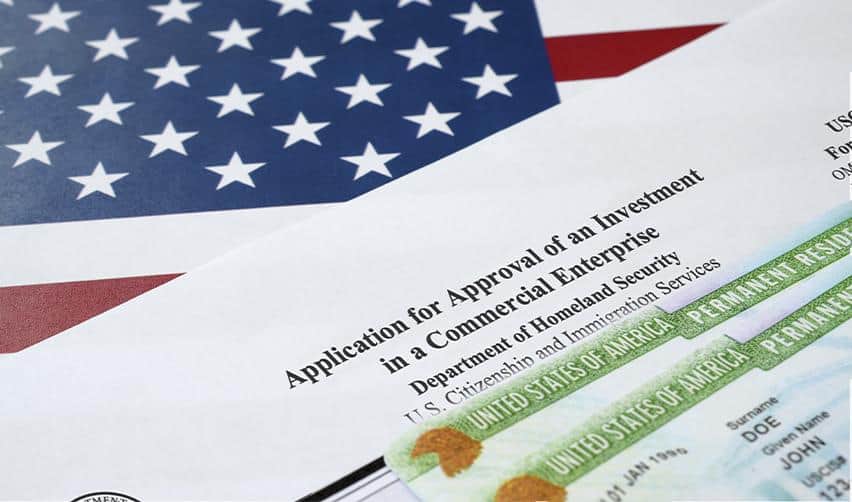 A close-up of an EB5 project approval form and a U.S. permanent resident card placed over an American flag.