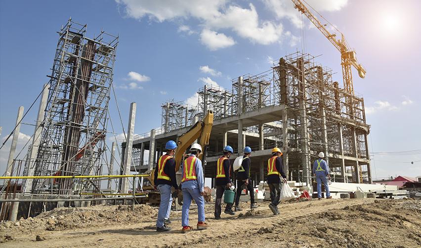 Construction workers in safety vests and helmets walking at an active building site with cranes and scaffolding, illustrating EB5 projects under development that create U.S. jobs.