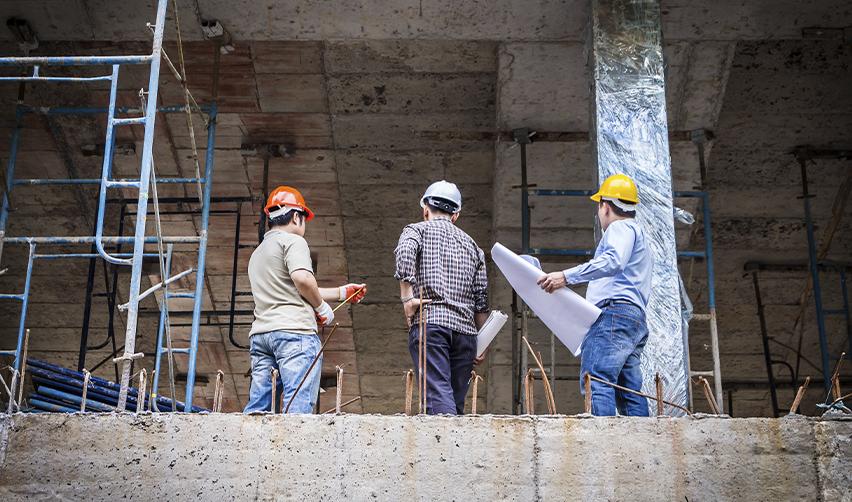 Construction workers wearing helmets reviewing blueprints at a building site, representing job creation in EB5 development projects.