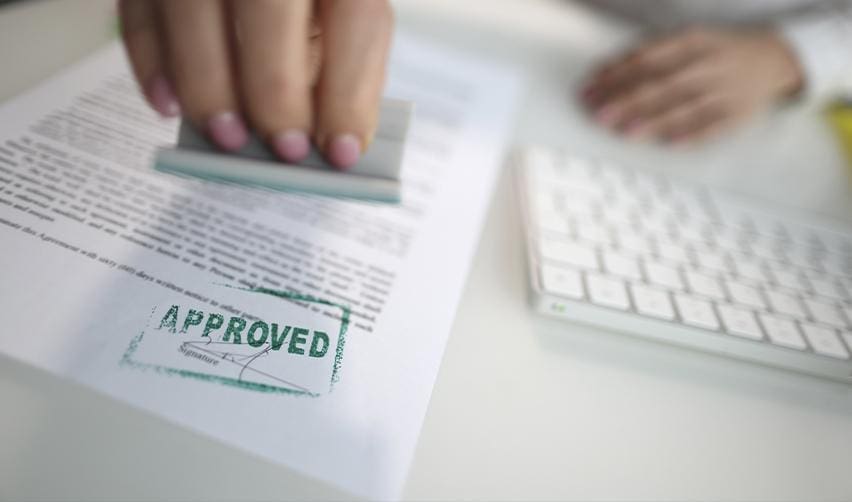 A person stamping an approved mark on official paperwork, representing USCIS review and approval of EB5 Form I956F project filings.