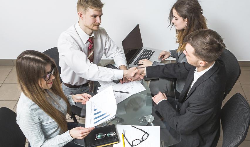 Business professionals shaking hands at a meeting table with financial charts and laptops, representing EB5AN’s due diligence and collaboration with trusted developers.