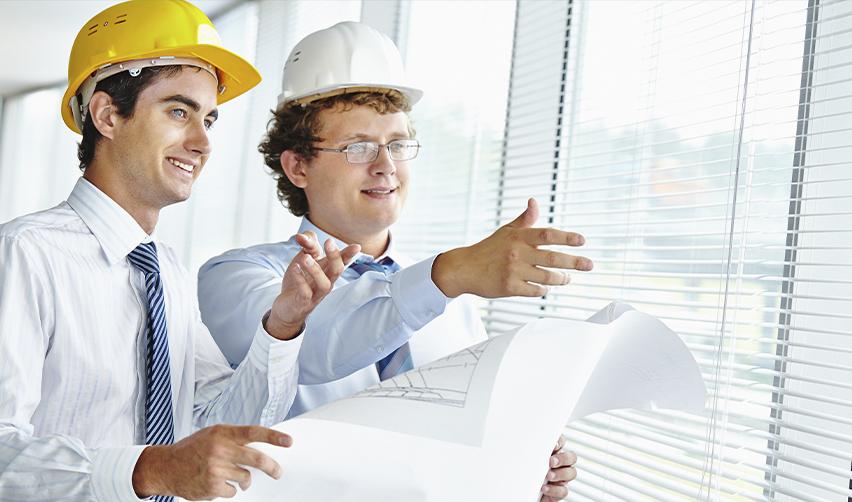 Two architects wearing hard hats reviewing blueprints in an office setting, symbolizing EB5 project design, planning, and compliance with USCIS requirements.