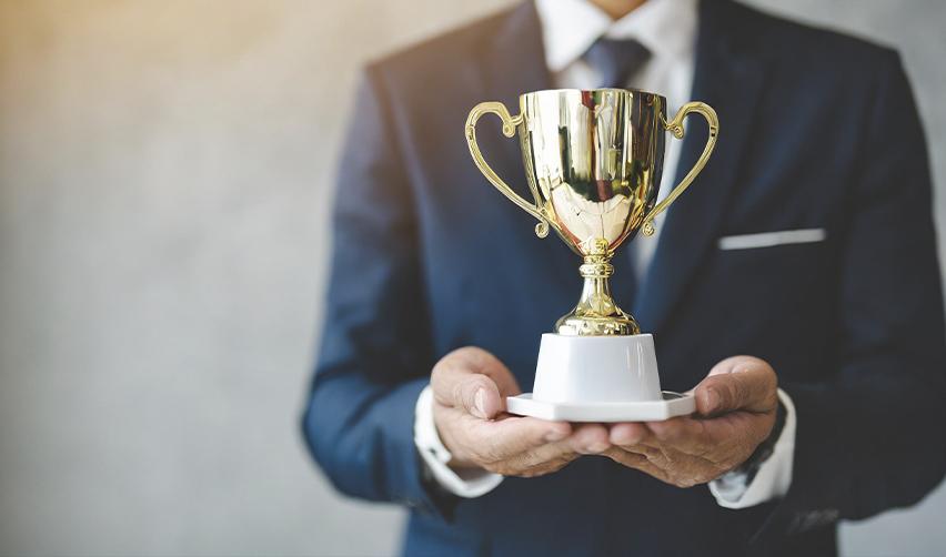 A close-up of a person in a suit holding a gold trophy, symbolizing Kolter Homes’ recent OBIE Awards for excellence in homebuilding, design, and marketing across its EB5AN sponsored active adult communities.