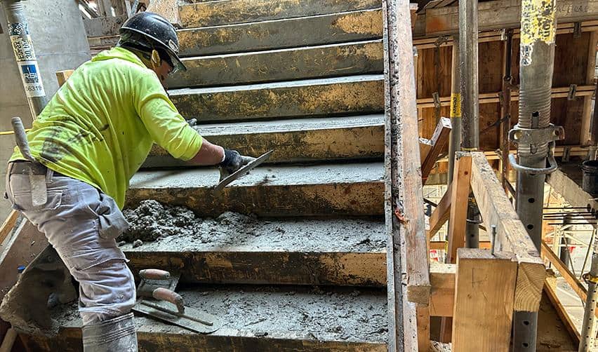 A construction worker smoothing fresh concrete on a newly formed staircase inside ONE Tampa, illustrating interior structural progress on the EB5 tower.
