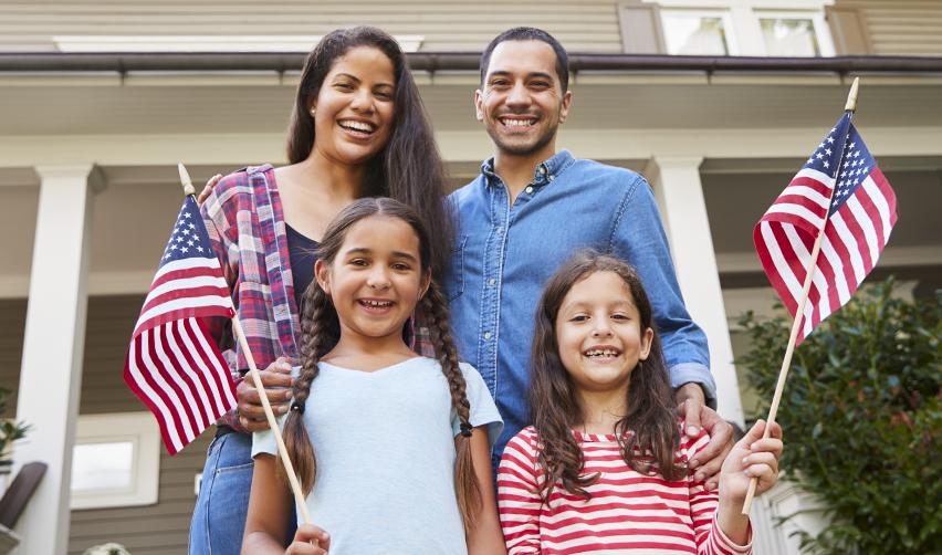 A family holding American flags in front of their home, symbolizing EB5 investors and their families obtaining U.S. permanent residency and long-term settlement.